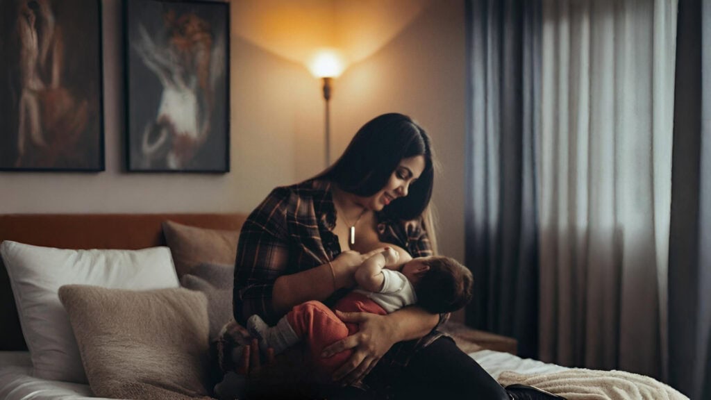 Mother breastfeeding her baby in a softly lit bedroom, creating a calm and nurturing moment