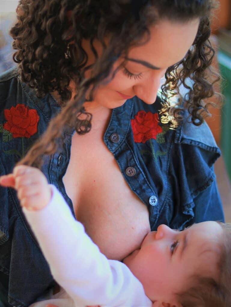 A mother lovingly breastfeeds her baby while gazing down with a smile, as the baby gently holds a strand of her hair—capturing the warmth, connection, and personalized care central to a private breastfeeding consultation.