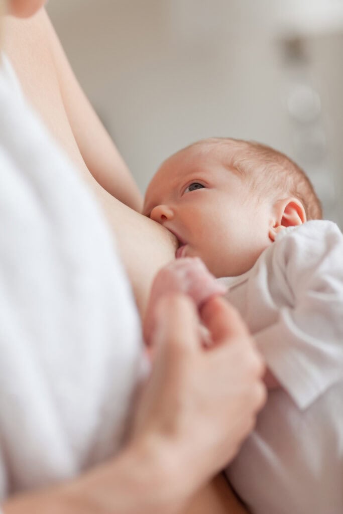 A newborn baby breastfeeding, closely latched onto the breast while being gently supported by a parent’s hand—demonstrating intimate bonding and proper positioning during a feed.