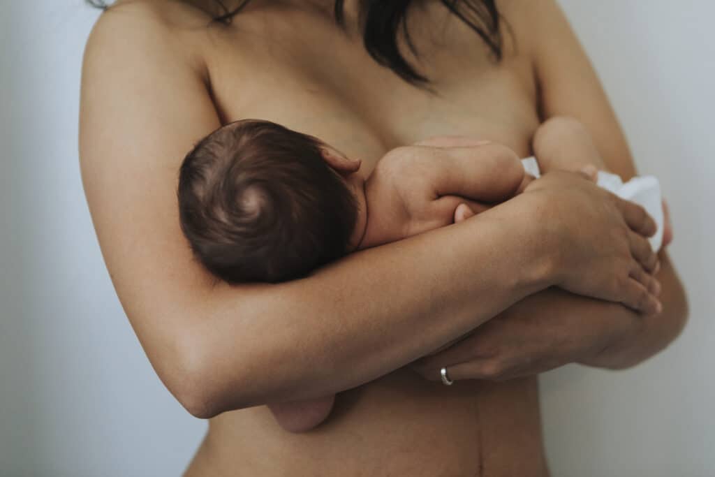 Naked mother holding her newborn baby against her bare chest, practicing skin-to-skin contact to support bonding and breastfeeding hormone release.