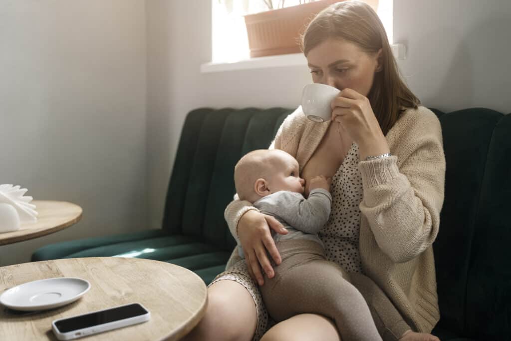 A mother sipping some tea holding a baby illustrating calm relaxation before feeding.