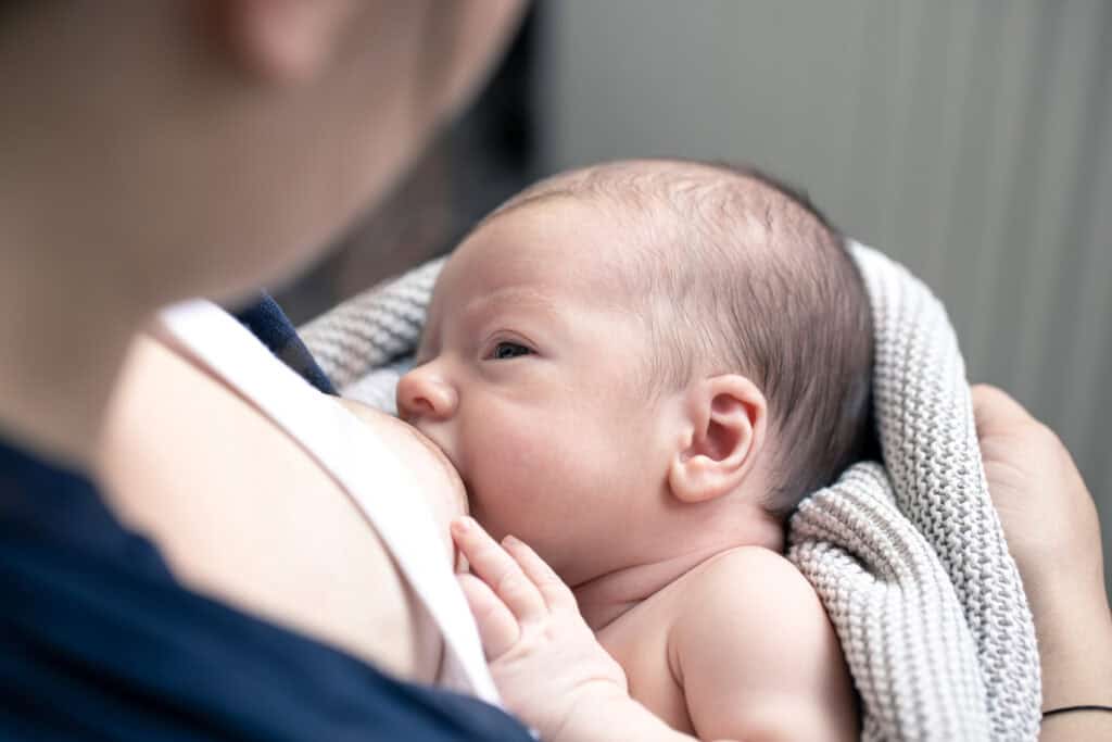 A mother, a baby showing a good latch on the breast during breastfeeding.