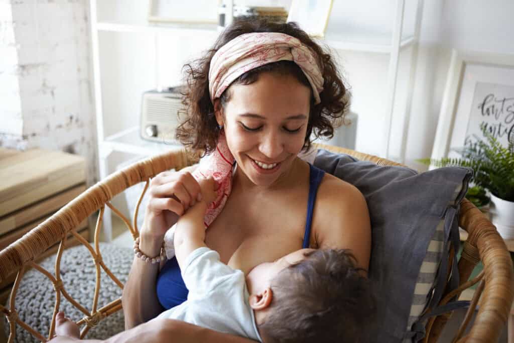 A mother smiling at her baby while breastfeeding during a cluster feeding session at home, a common part of growth spurts.
