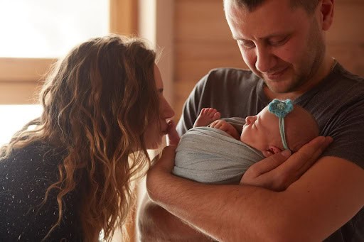A couple holding their child in the father's arms as the mother kisses the babies feet.